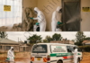 Technicians in protective suits fumigating mold indoors and spraying disinfectant around a vehicle outdoors